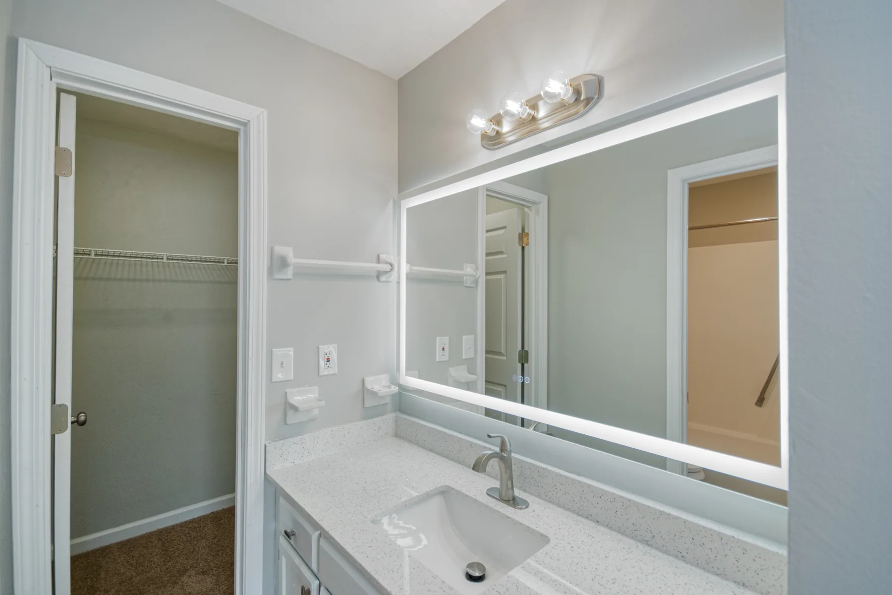 Bathroom vanity with large mirror and walk-in closet beyond at Castle Apartments