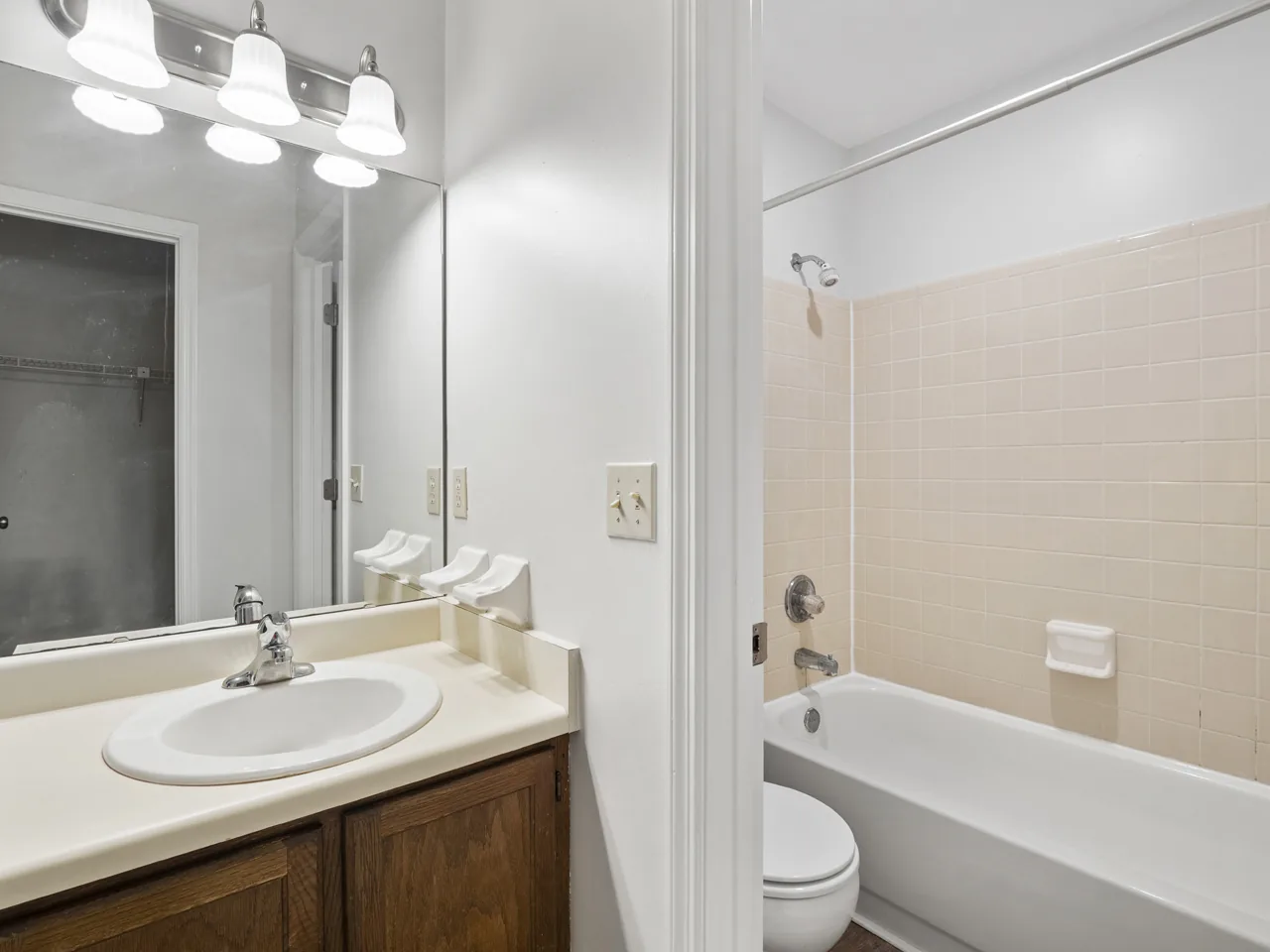 Classic bathroom with oak vanity, large mirror and tub shower at Castle Apartments