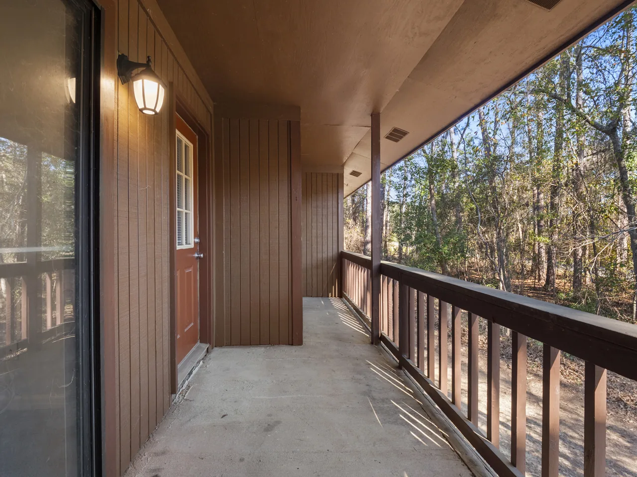 Covered private deck with wood railing overlooking trees at Castle Apartments