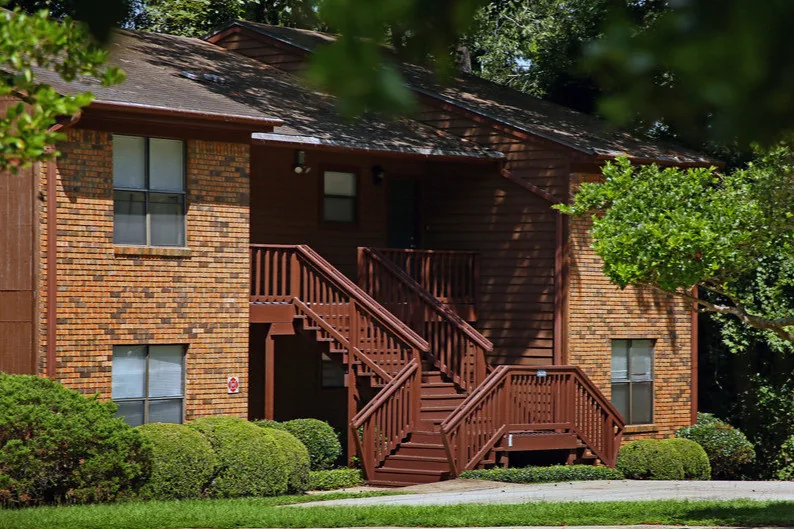 Brick apartment buildings with exterior stairs beneath large oak trees at Castle Apartments